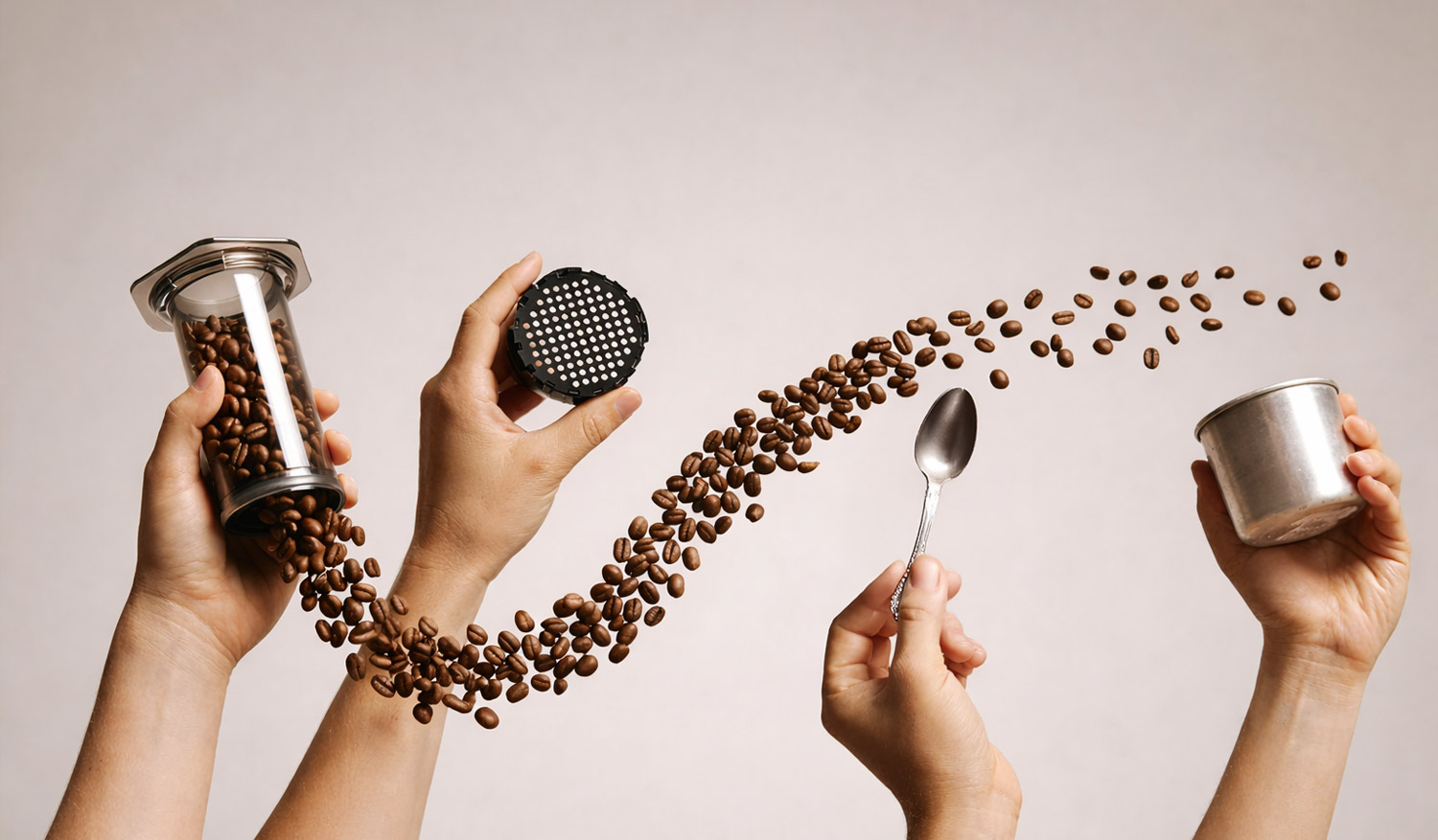 Mehrere Hände bereiten Kaffee zu: Kaffeebohnen fliegen in einer Bewegung von einem Behälter über einen Filtereinsatz und einen Löffel in einen Metallbecher vor neutralem Hintergrund.